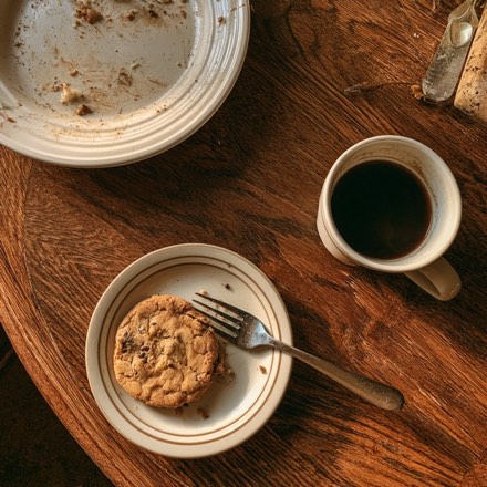 A chocolate chip cookie on a saucer beside a cup of coffee